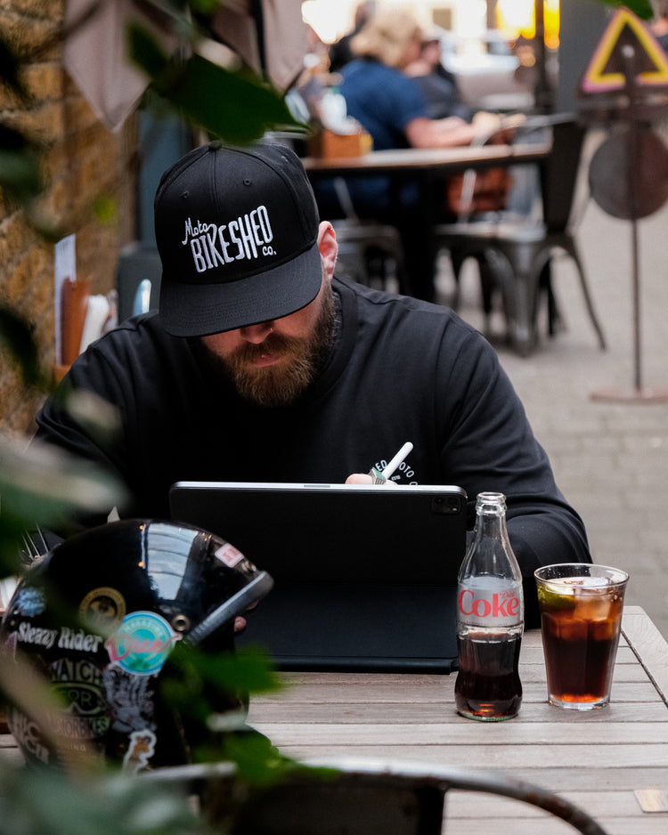 A black snapback baseball hat with 'Bike Shed Moto Co.' logo embroidered on the front.