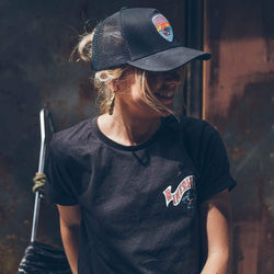 A black snapback baseball hat with a colorful patch on the front featuring a cartoonish motorcycle skull and bike shed logo - worn by a model