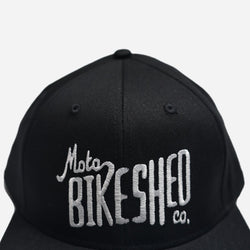 A black snapback baseball hat with 'Bike Shed Moto Co.' logo embroidered on the front detail