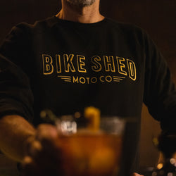 Bar staff member serving a drink wearing our BSMC Deco Motorcycle Sweatshirt - Black/Gold