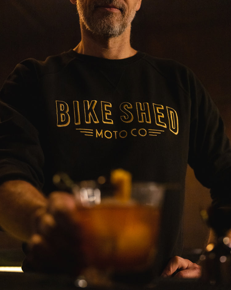 Bar staff member serving a drink wearing our BSMC Deco Motorcycle Sweatshirt - Black/Gold