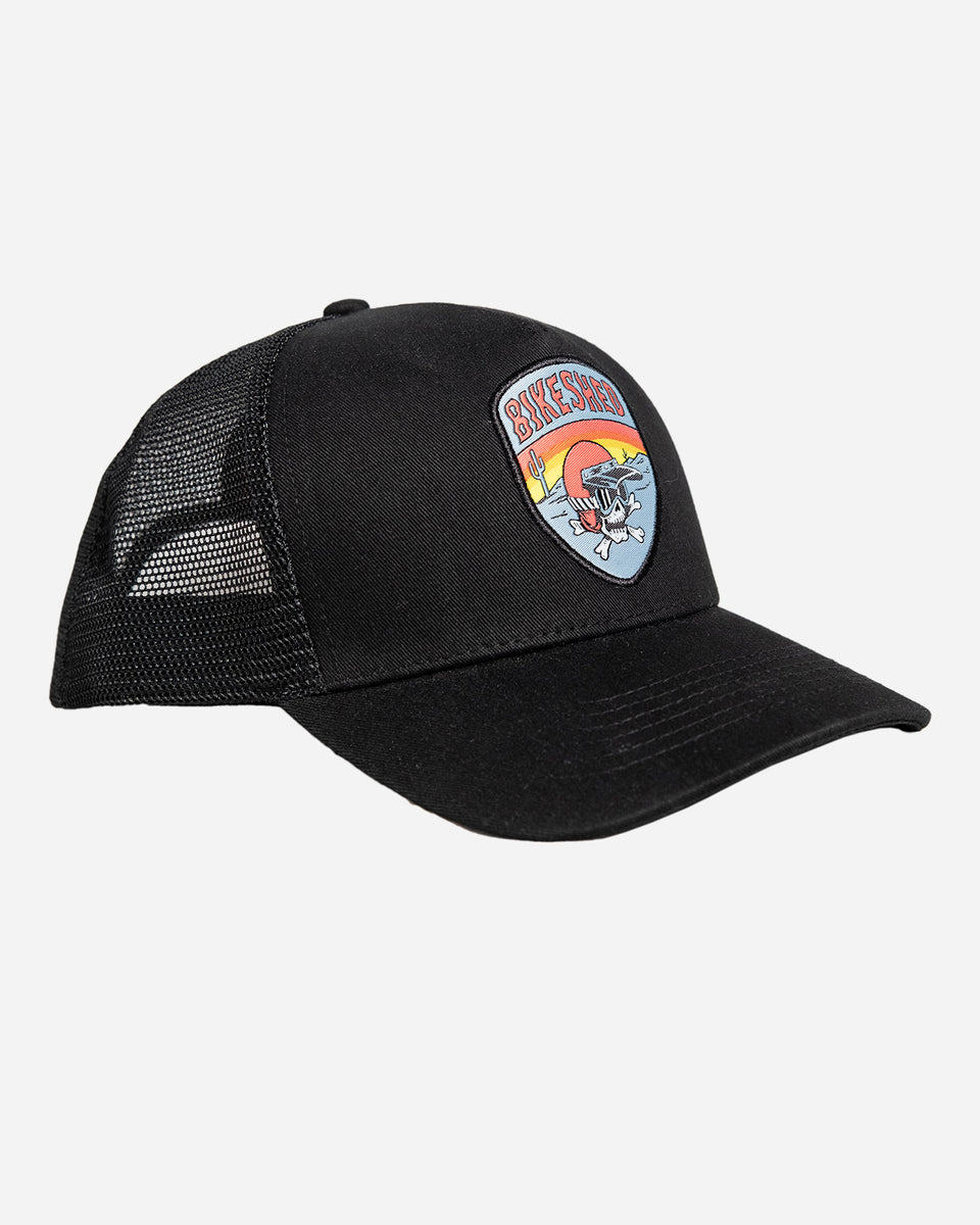 A black snapback baseball hat with a colorful patch on the front featuring a cartoonish motorcycle skull and bike shed logo - front