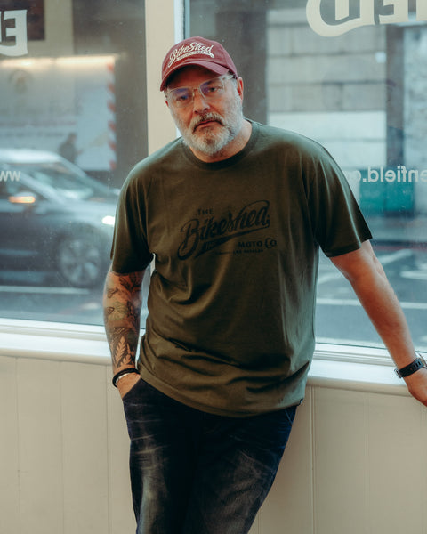 Model wearing Bike Shed Moto Co Inc T-Shirt Green in a white shop