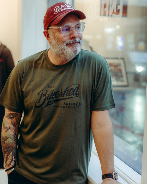 Model wearing Bike Shed Moto Co Inc T-Shirt Green in a white shop