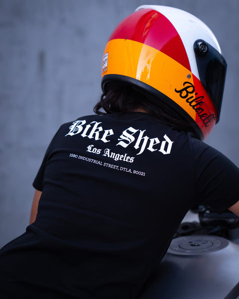 Model wearing Bike Shed Moto Co LA Rocker T-Shirt Black in front of a concrete back drop with a motorcycle 
