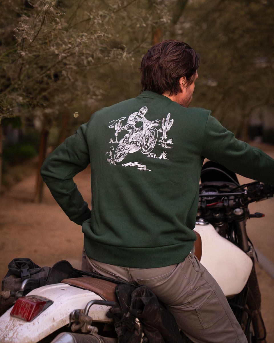 Model wearing Bike Shed Moto Desert Race Embroidered sweatshirt with a motorcycle in a dusty area