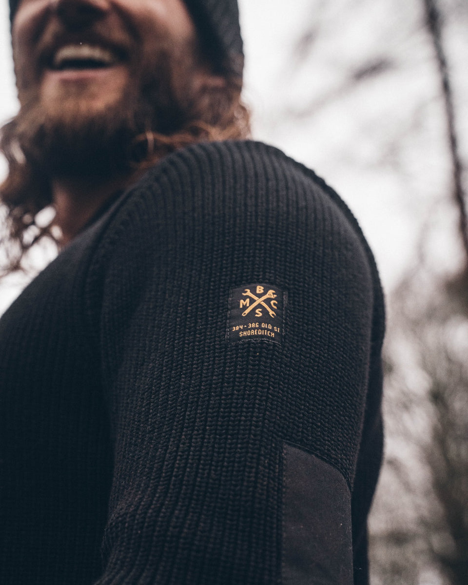 A black knit crew neck sweater with the Bike Shed Moto Co. brand label visible on the lower left side.