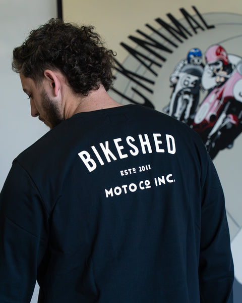 Model wearing Bike Shed Moto Co ESTD Long sleeve t-shirt in black in front of art work