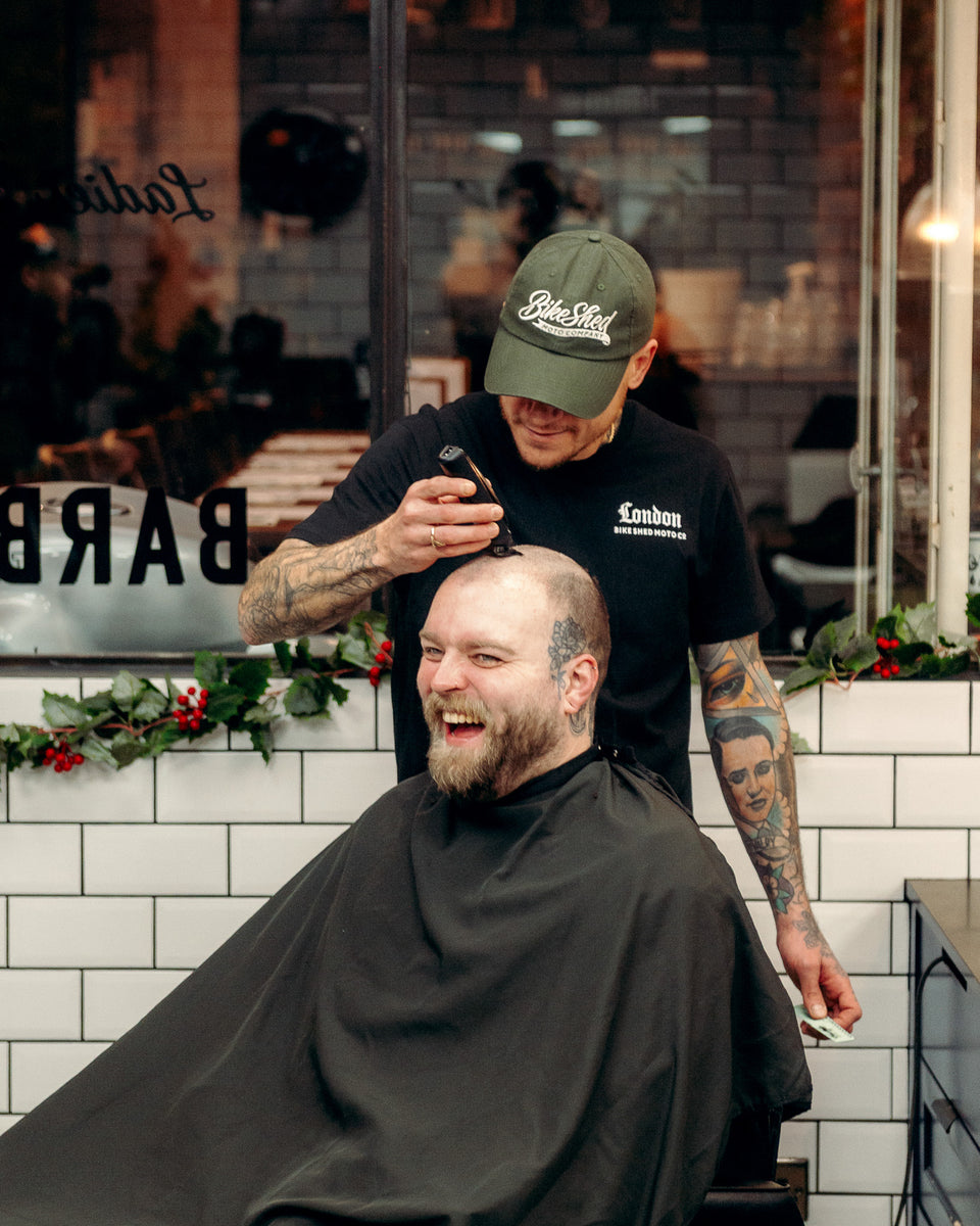 Model wearing Bike Shed Moto Script cap in green while cutting hair