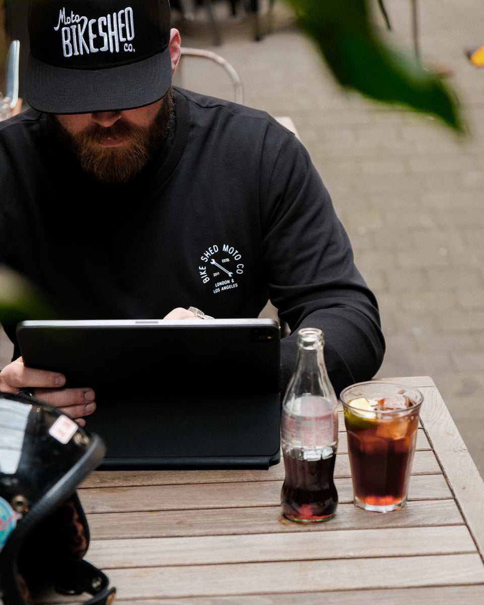 A long sleeve black T-shirt with a round neckline, featuring a front and back print. The front print is a logo, and the back print depicts an illustration of a motorcycle.