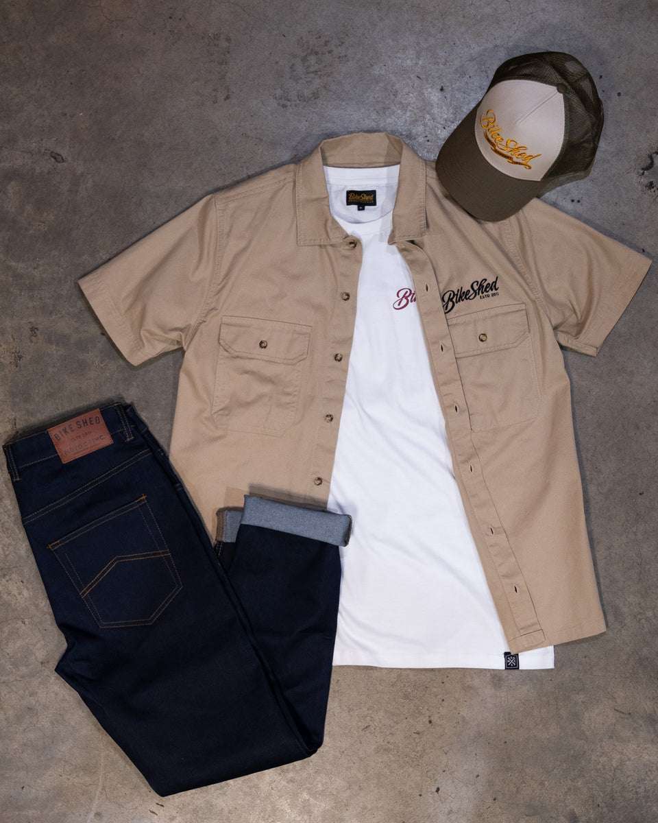 A beige Bike Shed Moto Co. Pennant shirt with button-up closure and chest pocket, featuring detailed embroidery on the chest and back.