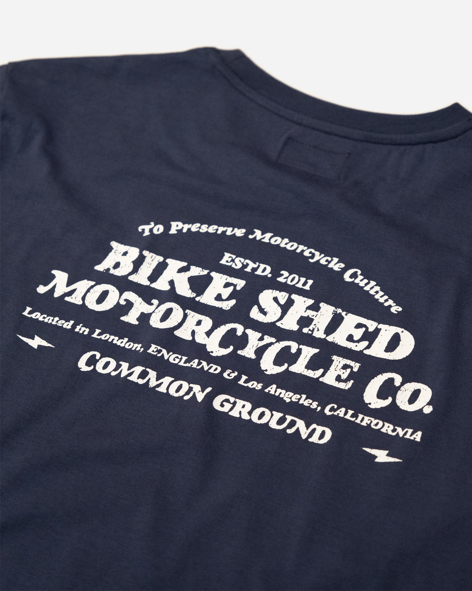 A navy-colored T-shirt with 'BIKE SHED MOTORCYCLE CO. COMMON GROUND' printed on the back.