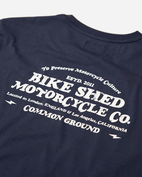 A navy-colored T-shirt with 'BIKE SHED MOTORCYCLE CO. COMMON GROUND' printed on the back.