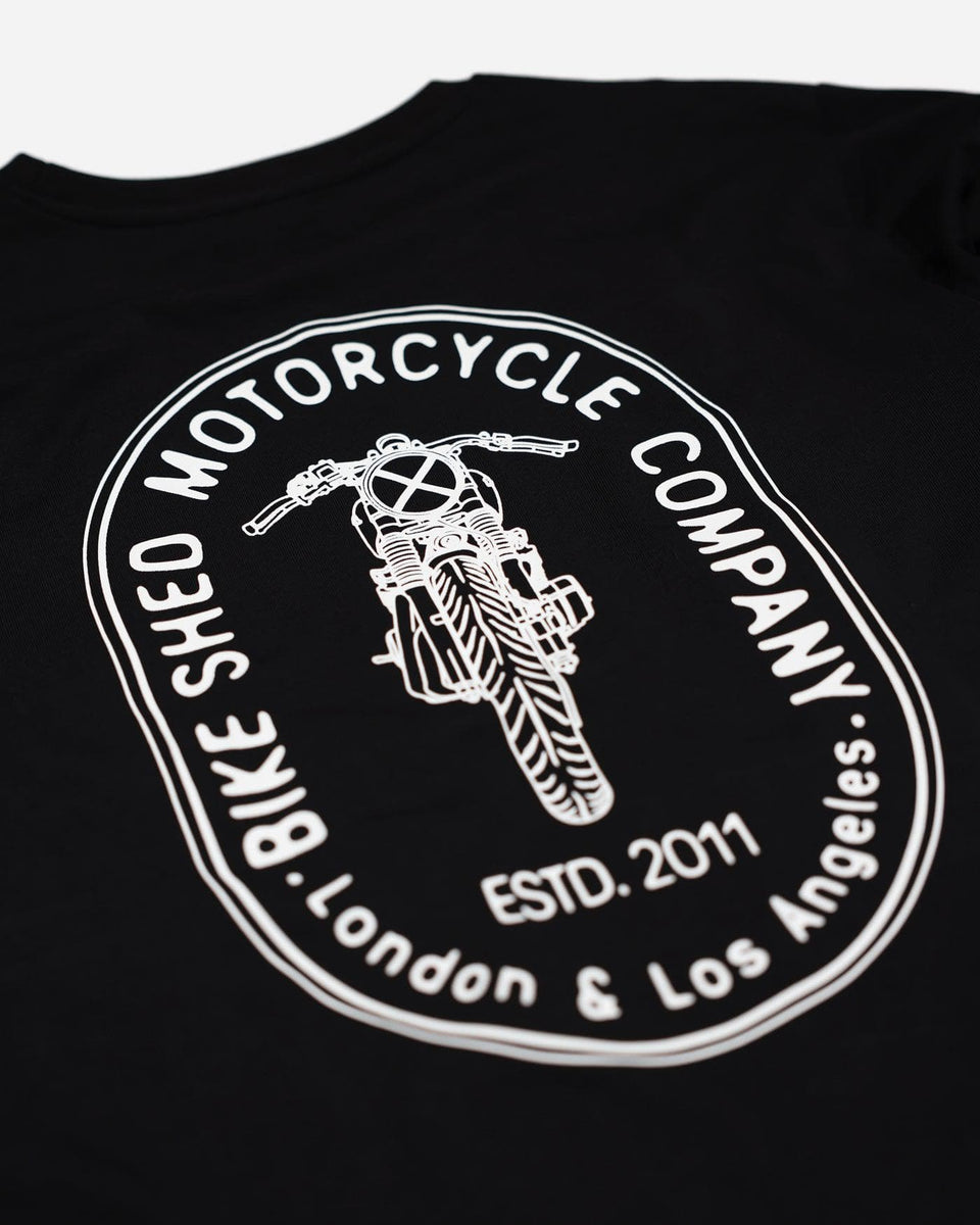 A long sleeve black T-shirt with a round neckline, featuring a front and back print. The front print is a logo, and the back print depicts an illustration of a motorcycle.