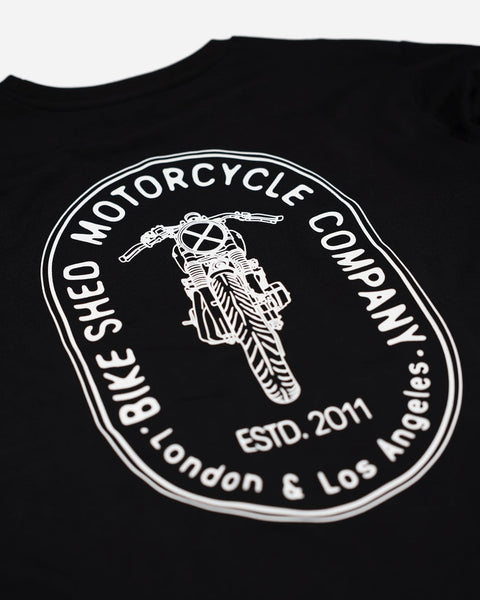 A long sleeve black T-shirt with a round neckline, featuring a front and back print. The front print is a logo, and the back print depicts an illustration of a motorcycle.