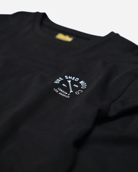 A long sleeve black T-shirt with a round neckline, featuring a front and back print. The front print is a logo, and the back print depicts an illustration of a motorcycle.