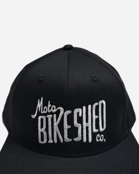 A black snapback baseball hat with 'Bike Shed Moto Co.' logo embroidered on the front detail