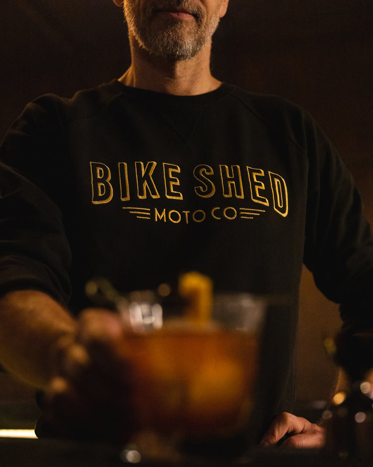 Bar staff member serving a drink wearing our BSMC Deco Sweat - Black/Gold
