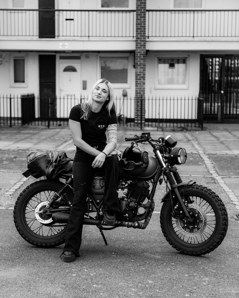Model sitting on her bike wearing our BSMC Women's ESTD. Pocket T Shirt - Black