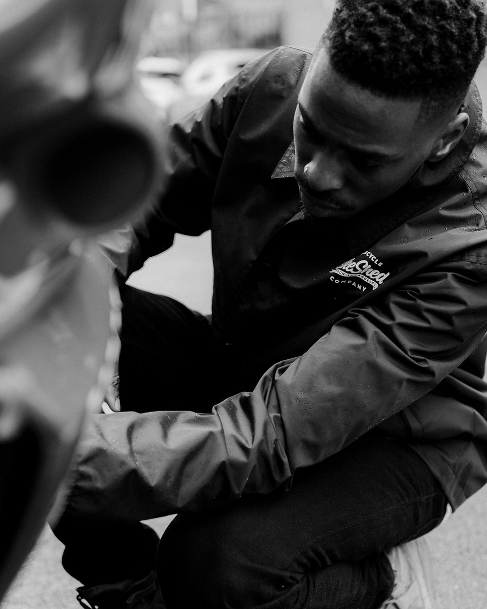 Model inspecting his bike wearing BSMC Company Coach Motorcycle Jacket - Black