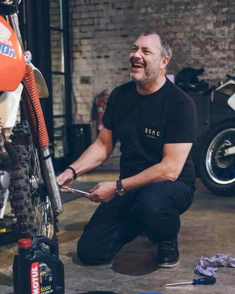 Dan working on his bike while wearing our Motorcycle BSMC ESTD. Pocket T Shirt - Black & Gold