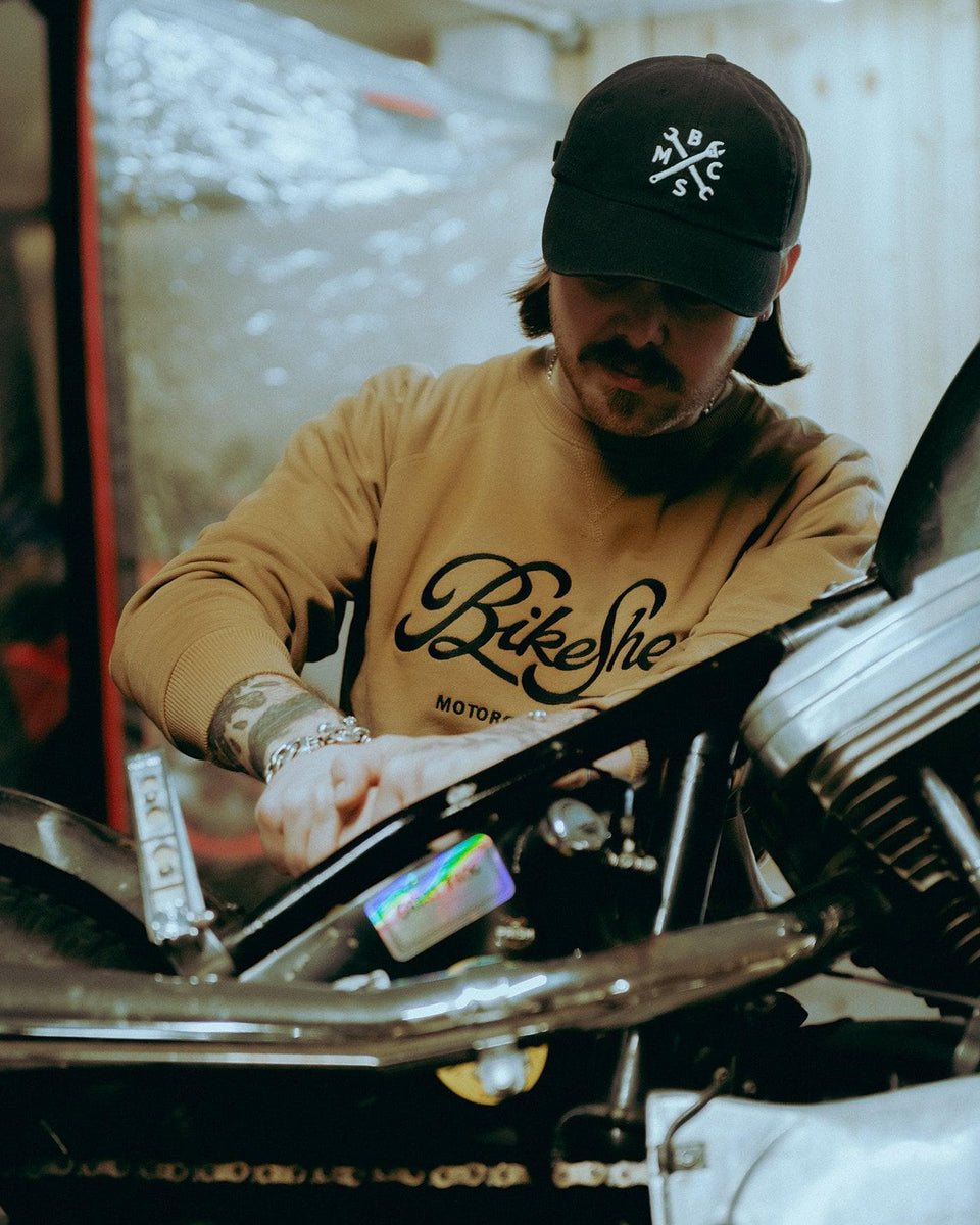 James working on his bike while wearing our BSMC Motorcycle Garage Sweatshirt - Tan/Black