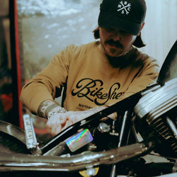 James working on his bike while wearing our BSMC Garage Sweat - Tan/Black