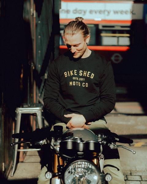 Steve sitting on his Triumph wearing our Bike Shed Motorcycle Logo Sweatshirt - Black/Gold