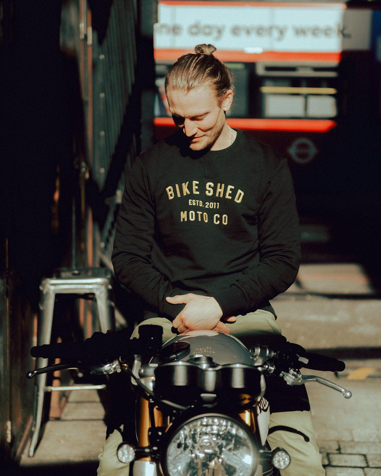 Steve sitting on his Triumph wearing our BSMC Moto Co. Sweat - Black/Gold